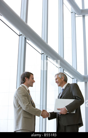 Two businessmen shaking hands in front of large glass windows Stock Photo