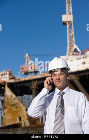 A construction engineer talking on his cellphone with an oil rig behind Stock Photo