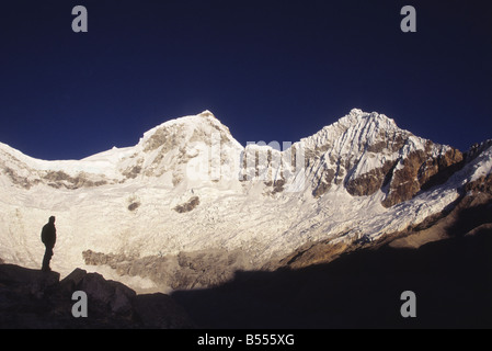 Trekker silhouetted below Mt Huandoy (L to R: East and North Peaks) looking at view, Cordillera Blanca, Peru Stock Photo
