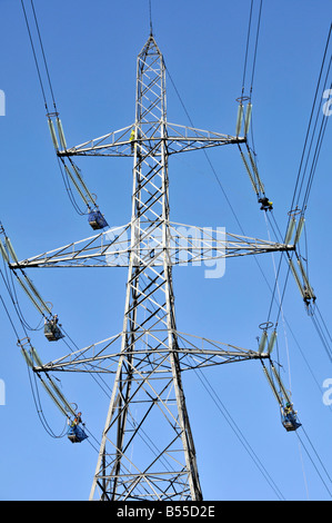 Group electrical engineers work on high voltage overhead electricity pylon power lines reached from cable trollies London 2012 Olympic site project UK Stock Photo