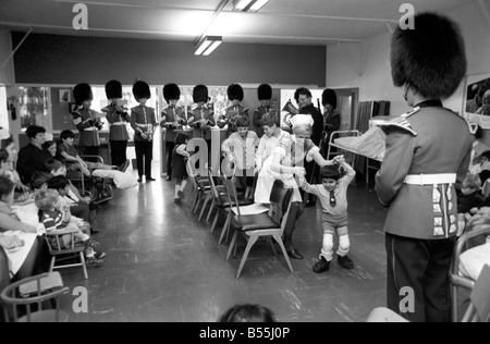 Part of the Coldstream Guards Band went to the children's ward at St. Thomas's London, and played their band music to the kiddies. The soldiers played Christmas Carols and happy marches. Some of the children even played some of the musical instruments. The nurses, children and soldiers joined in musical chairs. Then they all had tea, and the Tots Tattoo drew to a close. Leading the musical chairs is Hamid Shobali from Saudi Arabia who is being treated for deformity of the feet. The treatment is in the form of progress correction. December 1969 Z12127-004 Stock Photo