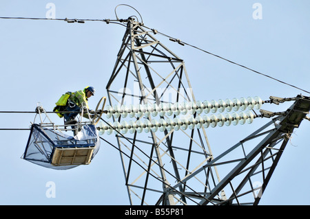 Close up Electrical engineer one of a team working from trolley cradle on high voltage power lines & pylons above Stratford East London England UK Stock Photo