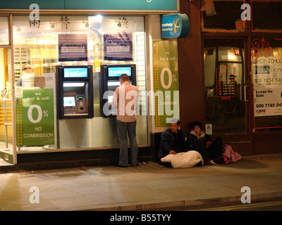 Financial crisis, hard times for some in 2008. Man getting cash from a Barclays ATM with beggars sitting next to it London UK Stock Photo