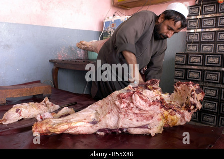 An Afghan butches carves meat off the leg of a cow in the town of Gardez, Paktia province, Afghanistan, October 2004 Stock Photo