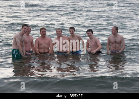 Group of 7 seven young men standing in the sea happy and smiling; summer holiday, wales UK Stock Photo