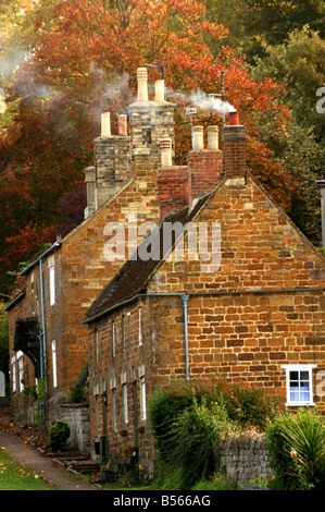 An ancient cottage with a smoking chimney in an autumnal setting Stock Photo