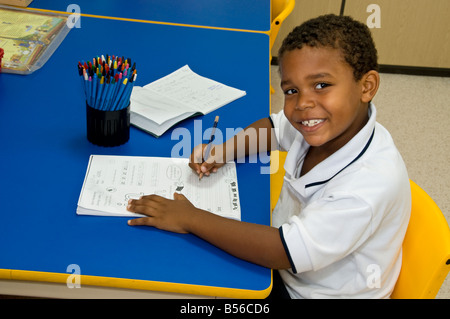 School boy infant African American 4-6 years confident happy black boy wearing uniform, learning to write at desk in kindergarten reception classroom Stock Photo