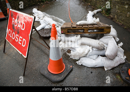Road closed sign due to flooding with sandbags directing water into manhole Wales UK Stock Photo