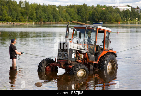 Tractor stuck in river and a man wading in water at river Oulujoki , Oulu , Finland Stock Photo