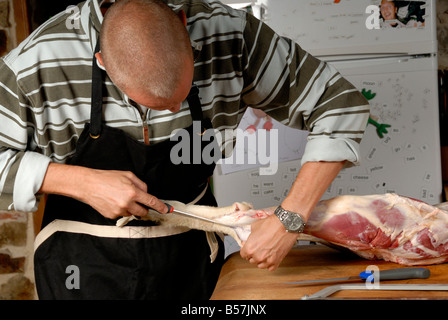 Stock photo of a man butchering a lamb in his Kitchen on a wooden table Stock Photo