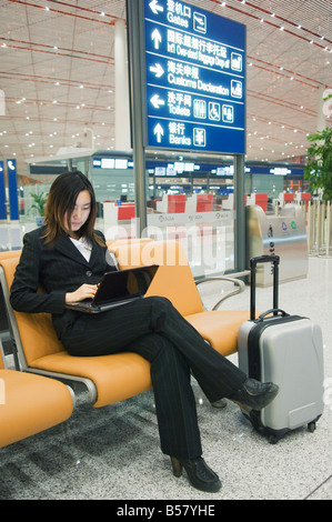 A Chinese business woman using a laptop computer at Beijing Capital Airport, Beijing, China Stock Photo