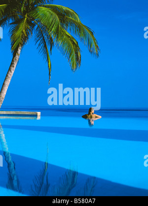 Woman in swimming pool under palm tree looking at sea, Maldives, Indian Ocean, Asia Stock Photo