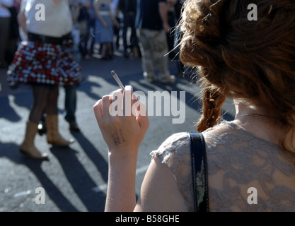 A young woman smokes a cigarette outside in a crowded area UK Stock Photo