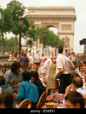 Greeting friends at an outdoor cafe on the Champs Elysees with the Arc de Triomphe behind Paris France Europe Stock Photo