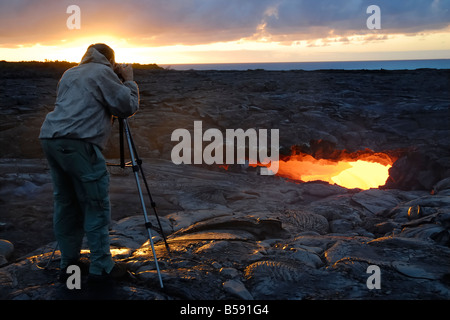 Hiker at sunrise Skylight and flowing lava Waikupanaha ocean entry lava flow Stock Photo