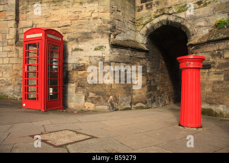 British red doric column style pillar/letter box and telephone box by stone arch entrance to Warwick town centre, England,UK Stock Photo