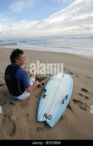 PORTRAIT OF A 50 SOMETHING MALE SITTING ON THE BEACH PREPARING TO GO SURFING  VERTICAL BDA11147 Stock Photo