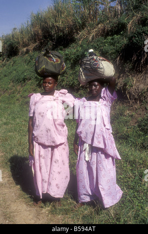 Two women carrying heavy head loads and wearing traditional long cotton dresses near Kabale in south west Uganda Stock Photo