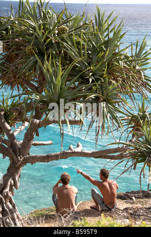 Two young men people sitting Pandanus palm tree pointing out sea Gorge Walk North Stradbroke Island Queensland QLD Australia Stock Photo