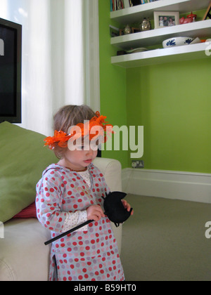 Little girl in pumpkin crown, leaning against a chair Stock Photo