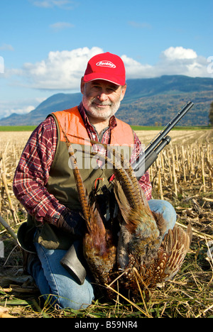 Upland game hunter with 12 gauge shotgun and brace of pheasant on fall day on Sumas Prairie cornfield Stock Photo