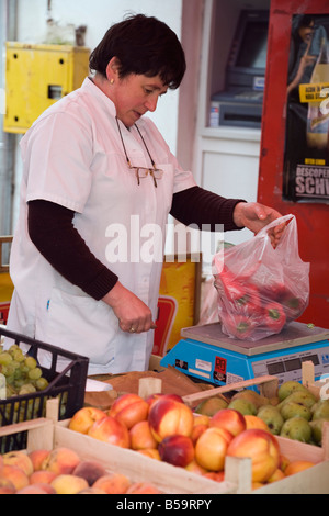 Woman shopkeeper weighing vegetables in grocery shop. Europe Stock Photo