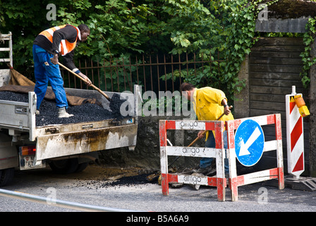 Two construction workers work on fixing holes in the road Stock Photo