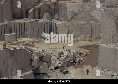 Men walking past clean faces for block extraction in granite quarry Budduro Sardinia Italy Europe Stock Photo