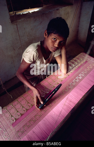 Young boy looking unhappy sitting at loom working on silk material with gold thread India Asia Stock Photo