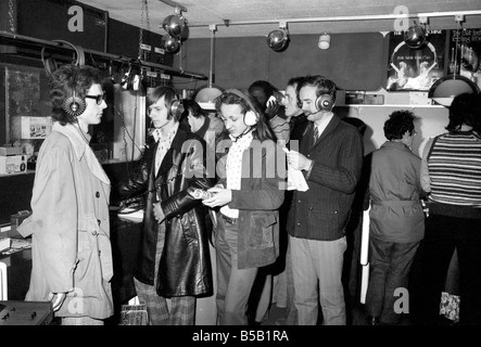 Beat the Budget shopping spree in Tottenham Court Road, London, street of radio and Hi-fi. ;Customers trying on headphones in an electrical store;April 1975 ; Stock Photo