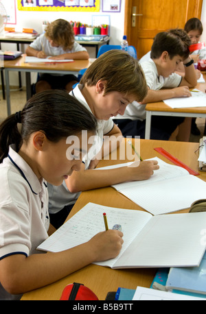 Junior school children concentrate on their exam writing at class desk in school classroom Stock Photo