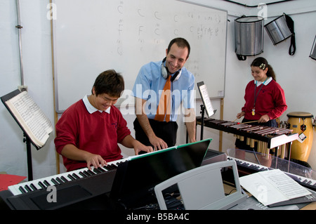Two teenage students in music class playing electric piano and xylophone with teacher Stock Photo