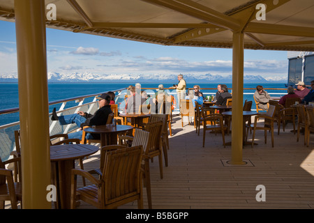 Cruise passengers visiting on outdoor dining deck watching snow capped mountains on Inside Passage cruise in Alaska Stock Photo