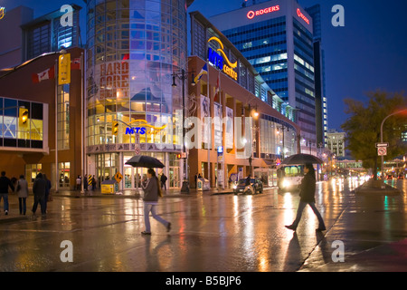 Pedestrians crossing a city street on a rainy night, carrying umbrellas, Portage Avenue, Winnipeg, Manitoba, Canada. Stock Photo