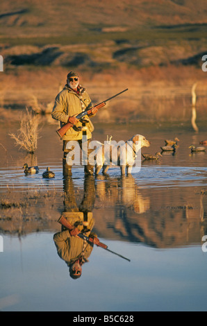 A duck hunter with a Labrador Retriever dog is reflected in a calm shallow lake in late afternoon near Caballo Lake, southern New Mexico. Stock Photo