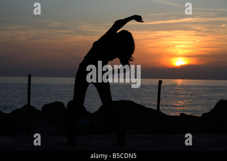 Young woman silhouette stretching at sunset Stock Photo
