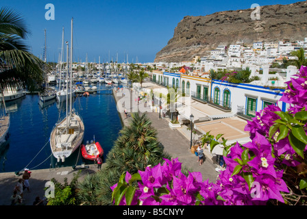 Puerto de Mogan overview shops restaurants bars viewed over bougainvillea flowers, to yacht marina and promenade. Gran Canaria Canary Islands Spain Stock Photo