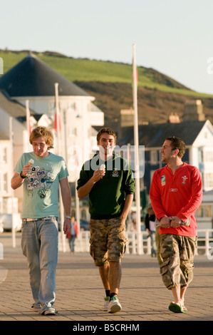 Three young men university students walking and eating icecream on the promenade Aberystwyth Wales UK summer evening Stock Photo