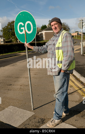 Man controlling traffic with a hand held rotating stop go sign on pole at roadworks Stock Photo