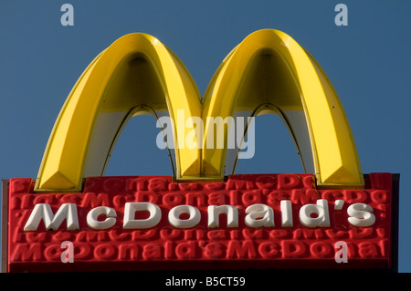 McDonald s fast food restaurant sign yellow golden arches symbol against clear blue sky, UK Stock Photo