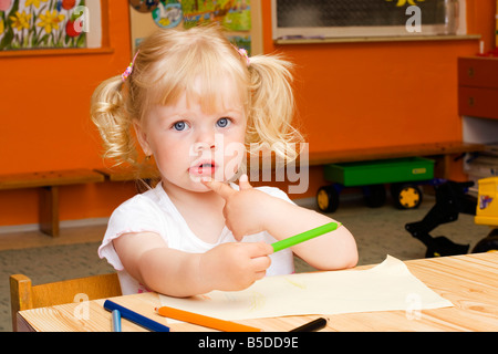 Blond little girl, 2 years, sitting at table with crayons Stock Photo