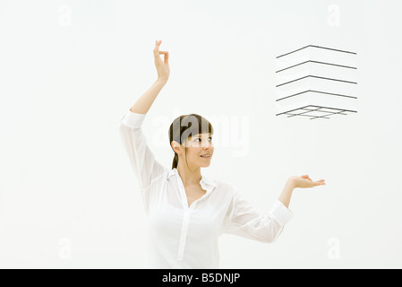 Woman raising arms, looking up at cube floating in midair Stock Photo