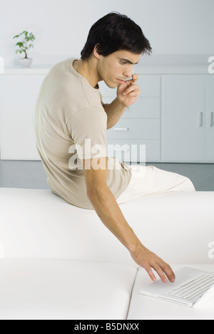 Man sitting on top of couch, using laptop and cell phone Stock Photo