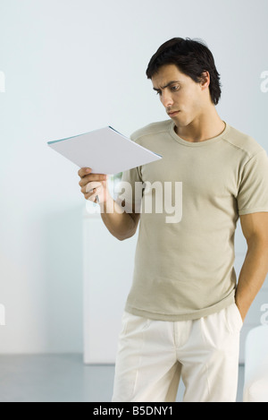 Man standing with hand in pocket, reading document, frowning Stock Photo