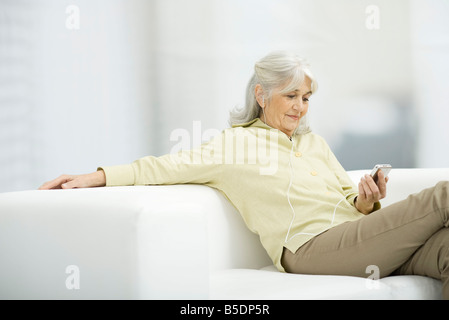Senior woman listening to MP3 player, sitting on couch Stock Photo