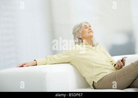 Senior woman listening to music, sitting on couch with eyes closed Stock Photo