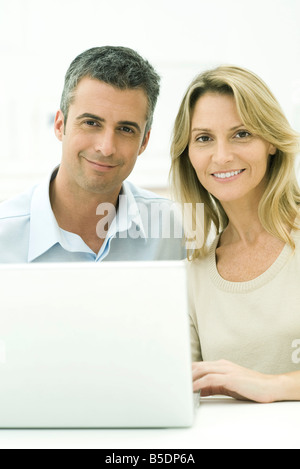 Couple sitting together with laptop, smiling at camera Stock Photo