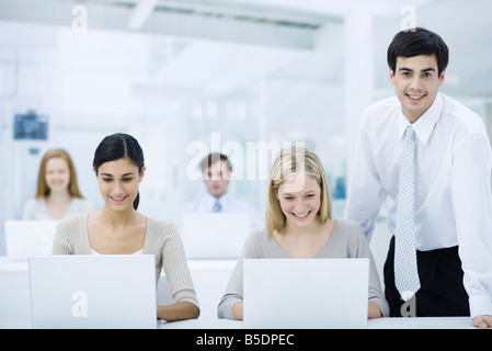 Supervisor standing beside employees working on laptops, smiling at camera Stock Photo