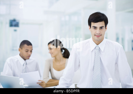 Businessman in office, smiling at camera, employees working in background Stock Photo