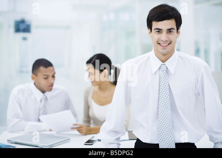 Businessman smiling at camera, colleagues working in background Stock Photo